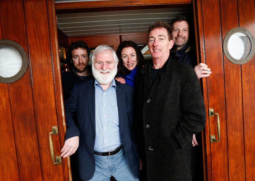 John sheahan stands aboard a wooden boat with other musicians