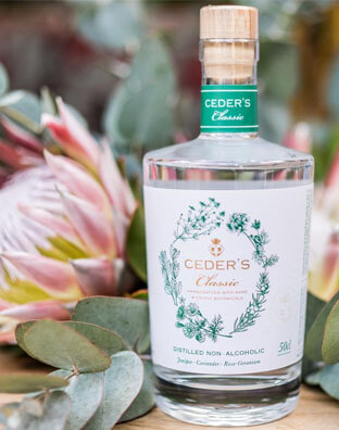 a glass bottle of ceder's gin sits among green and pink flowers