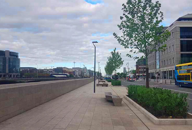 a newly paved walkway on georges quay with benches, tress and hedging