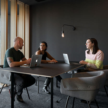 three people with laptops sit around a table in a modern office and brainstorm about starting a business
