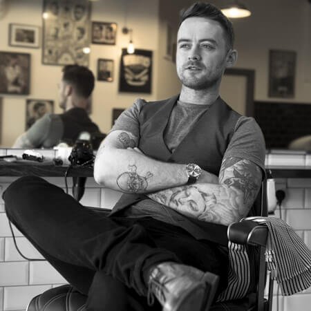 sean bryan of cut & sew sit on a barber chair with his arms folded