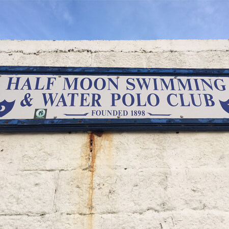 blue and white sign of the half moon swimming club on white brick wall