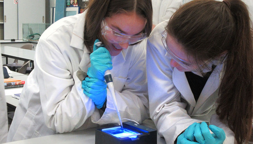 two female pupils from st andrew's private school wear lab coats and goggles