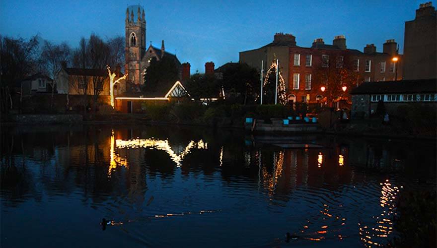 the lights on the blessington basin lodge reflect in the water of the duck pond at night