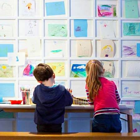 two children stand in front of colourful art and postits that line the walls of the ark