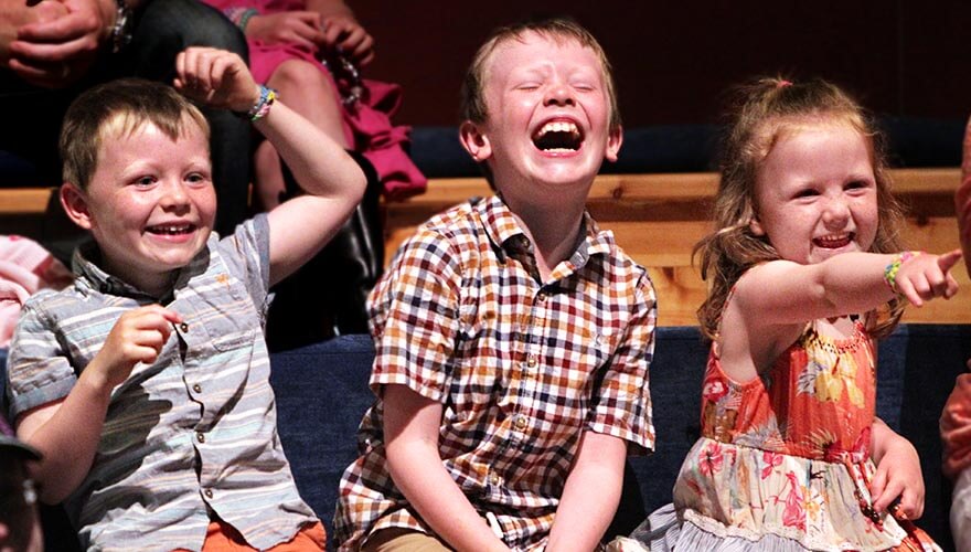 three children laugh and point at a performance in the ark