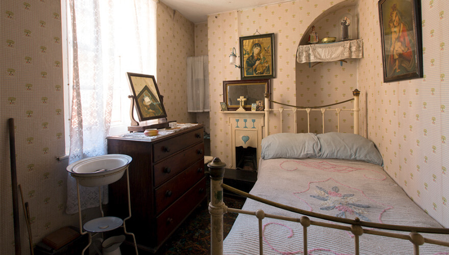 a bedroom with a metal bed frame, holy pictures and a washing basin