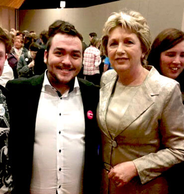 lgbtq student sean frayne wears a shirt and blazer as he poses for a photo with mary mcaleese