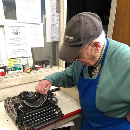 in a cap and apron, joe millar senior looks at a black typewriter