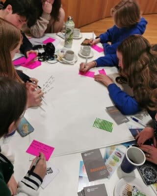 members of comhairle na nóg sit around a table in school jumpers brainstorming on large sheets of paper