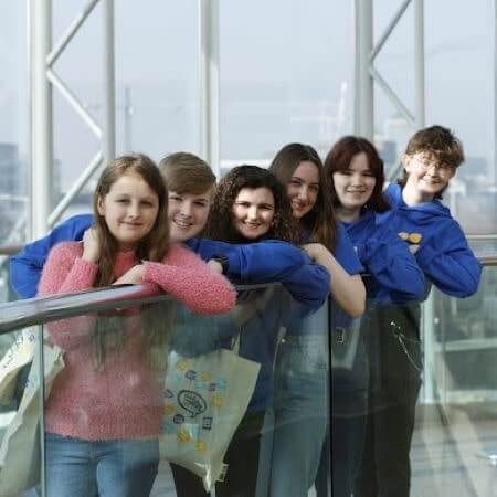 members of comhairle na nog stand in a line leaning on an elevator to pose for a photo